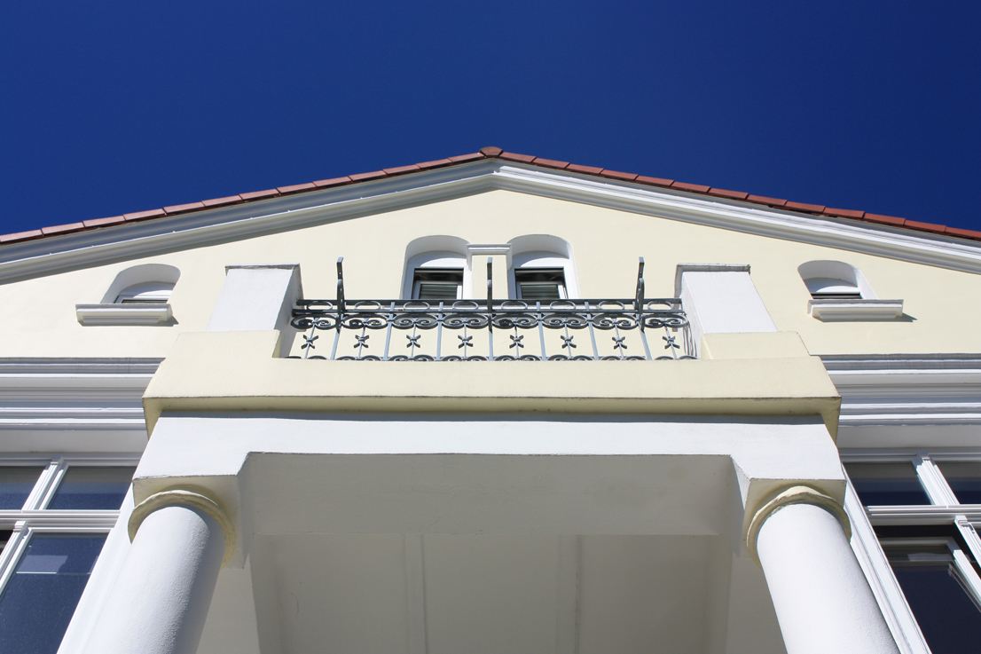Balkon der Villa mit schmiedeeisernem Geländer vor blauem Himmel