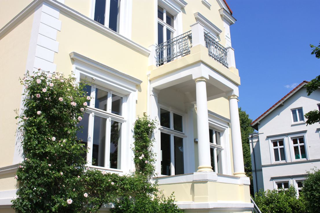 Gelbe Gründerzeit-Villa mit weißem Stuck und Rosen am Eingang